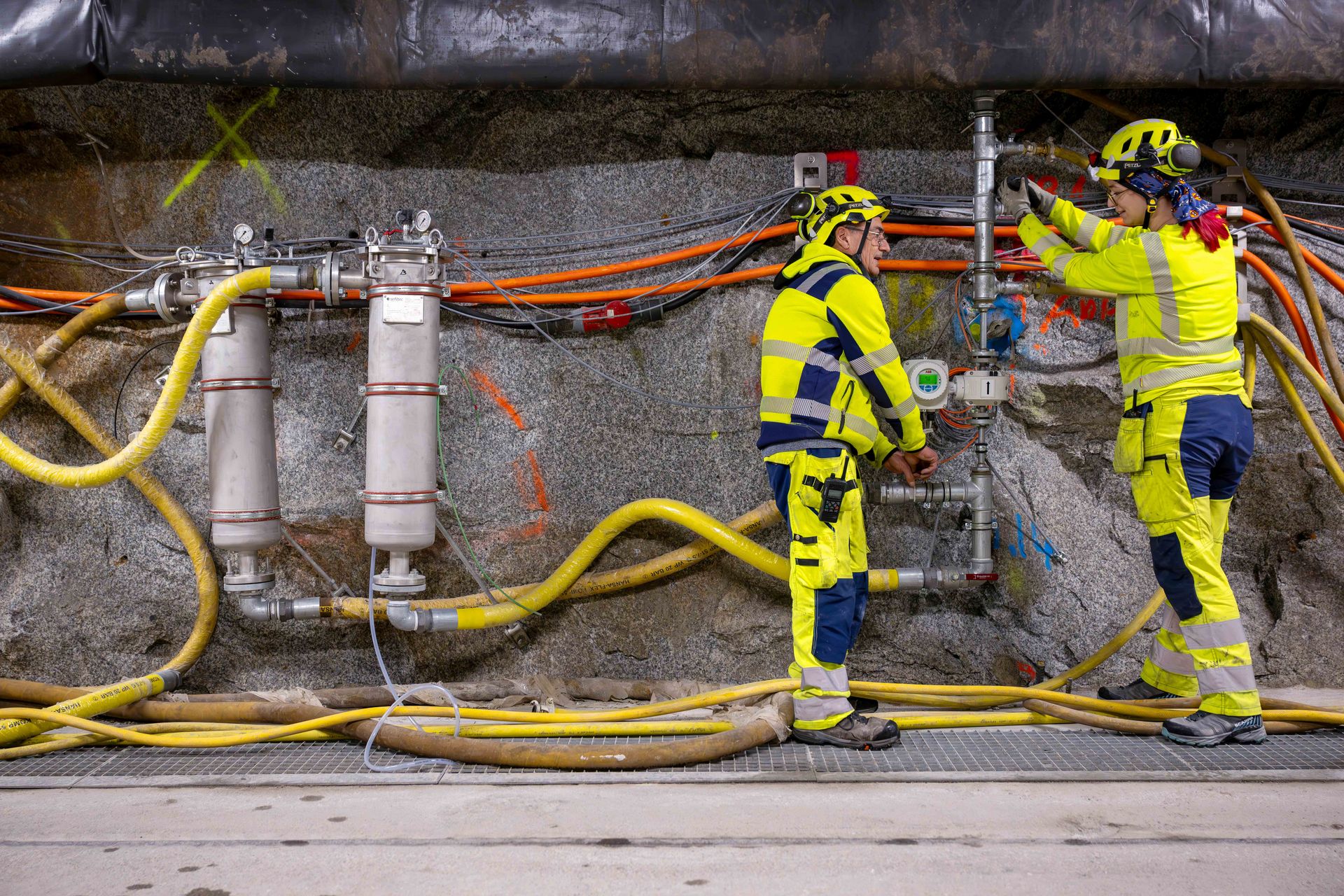 Das Bedretto-Untergrundlabor ist vollgepackt mit Pumpen, Sensoren und Leitungen, die für die zahlreichen Forschungsprojekte benötigt werden. Zwei Forschende im Bedretto-Untergrundlabor