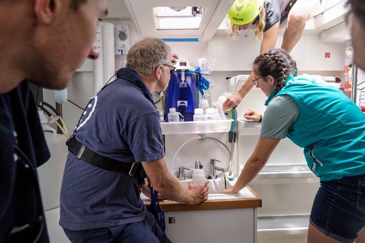 The interns observe the fixation procedure for the plankton sample, while oceanographer Hedy Aardema performs an acrobatic feat to reach for a filling hose (top of photo).